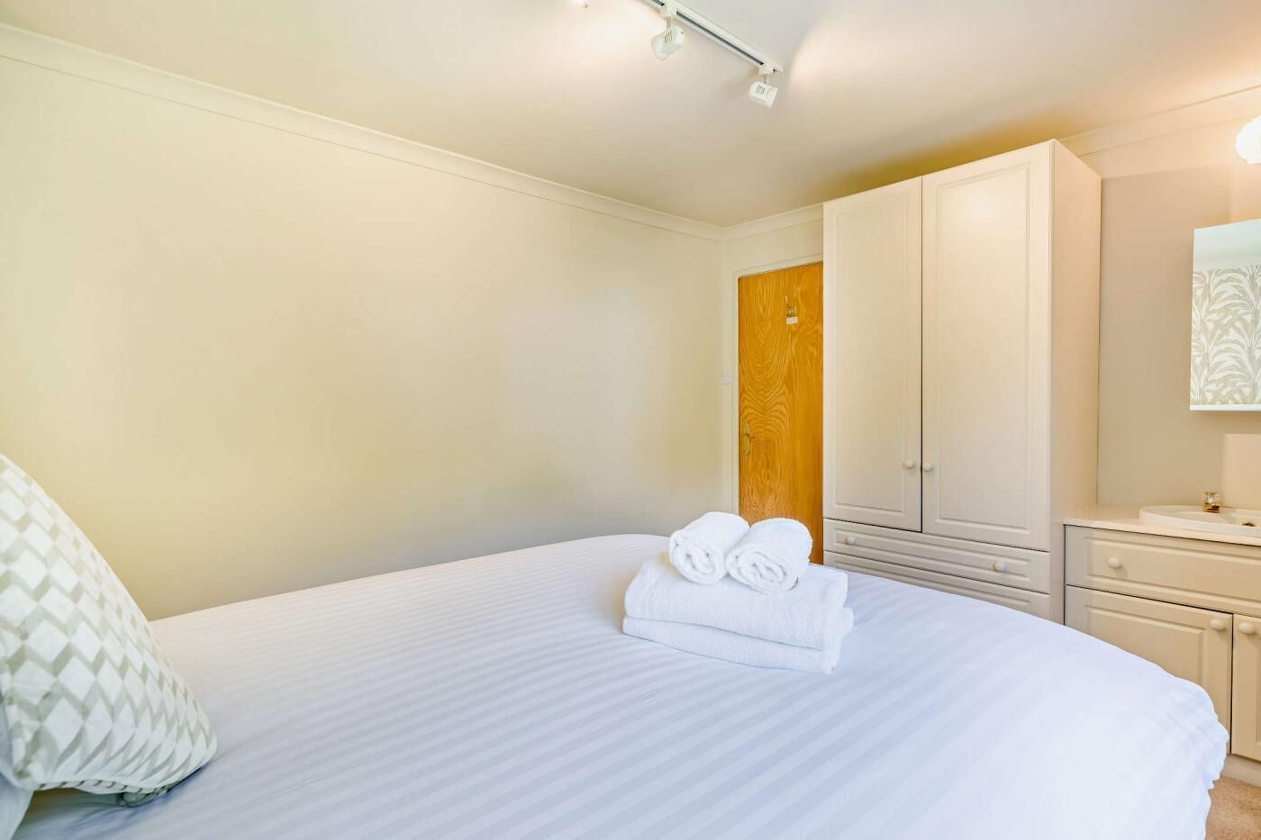 A hotel room with a large bed, a wooden door, and a white wardrobe.