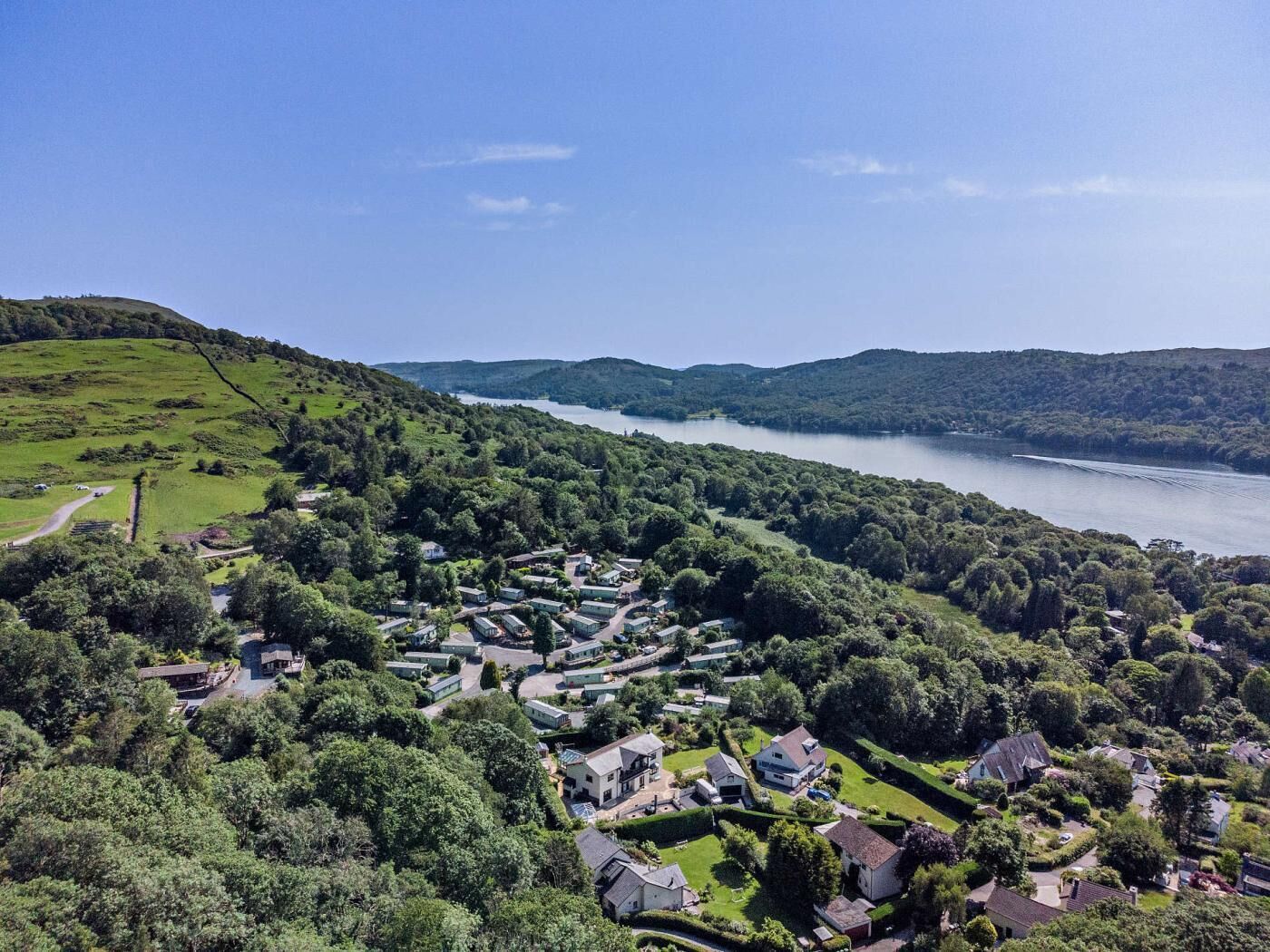 A residential area with houses surrounded by lush greenery and a lake in the background.