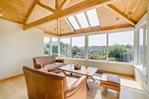 A spacious room with a high ceiling, large windows, a leather sofa, a coffee table, and a view of a green landscape. - 3 Bed in Windermere (oc-f31899) (Tower Wood)
