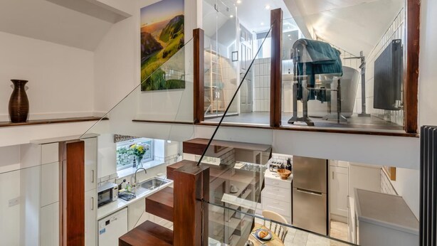 A modern interior with a glass staircase, a kitchen with white cabinets, and a dining area with a table and chairs.