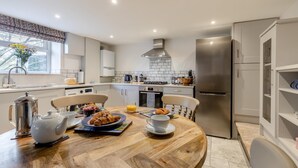 A modern kitchen with a dining table set for breakfast, a refrigerator, and a window with a view.