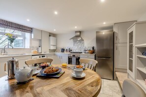 A modern kitchen with a dining table set for breakfast, a refrigerator, and a window with a view.