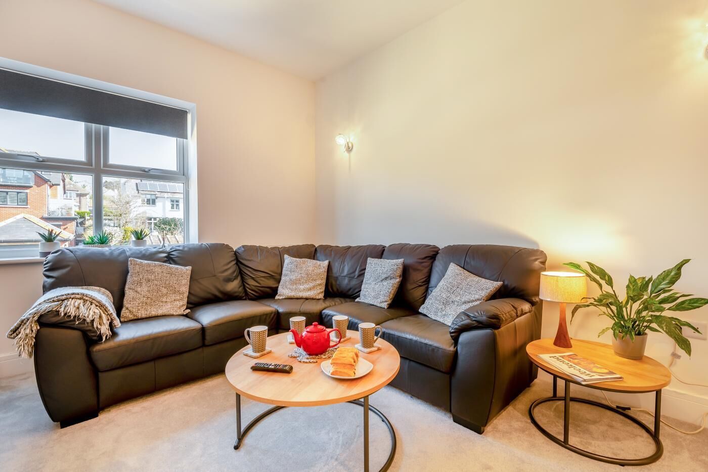 A modern living room with a leather sectional sofa, a round coffee table, and a side table with a lamp and a plant.