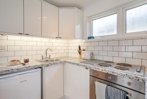 Kompakti keittiö, jossa on valkoiset kaapit, sisäänrakennettu uuni, liesi ja ikkuna tiskialtaan yläpuolella.