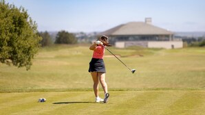 Camp de golf amb un jugador amb samarreta vermella i falda negra, un club de golf i pilotes de golf sobre l'herba.