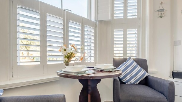 A dining area with a round table, two grey armchairs, and a vase with flowers. - 1 Bed in Sheringham (oc-n31825) (Sheringham)