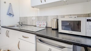 A modern kitchen with white cabinets, a stainless steel kettle, a microwave, and a dish drying rack. - 1 Bed in Sheringham (oc-n31825) (Sheringham)