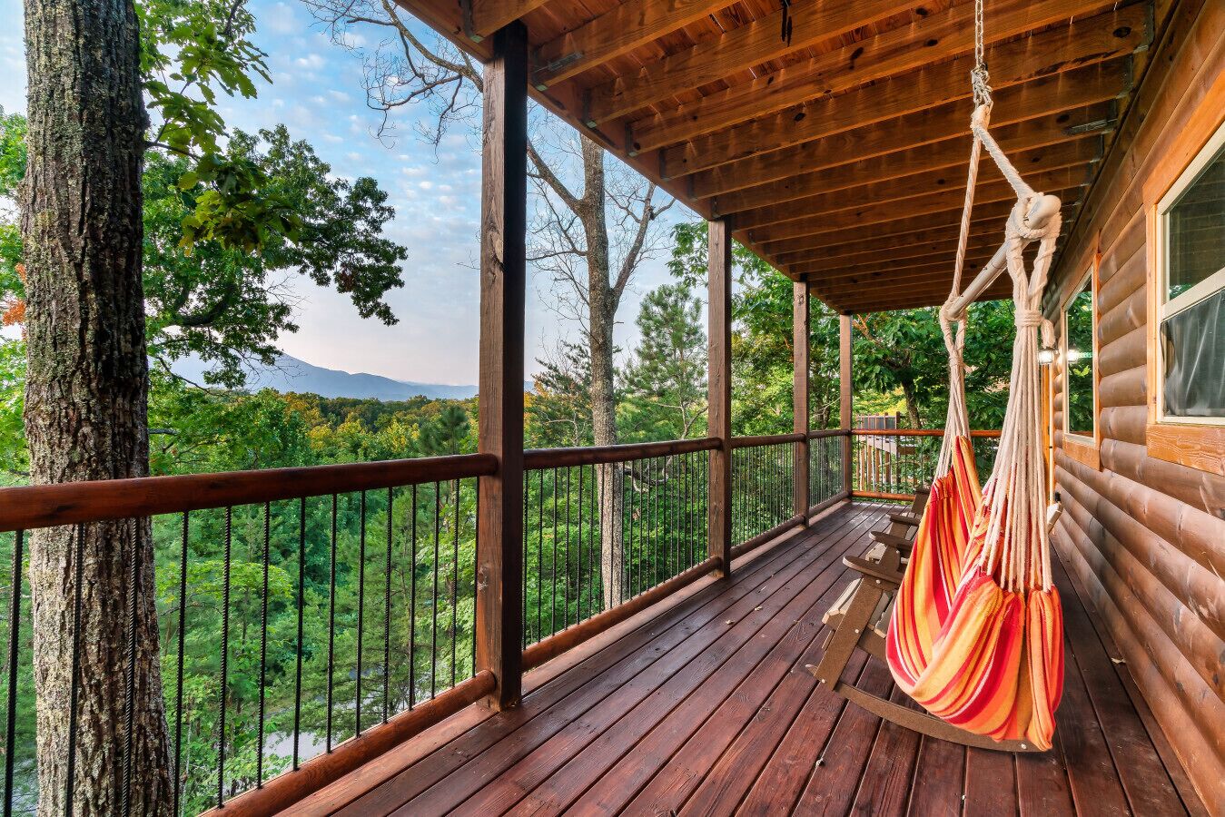 A wooden deck with a hammock, overlooking a forested area.
