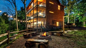Une cabane en bois à plusieurs niveaux, dotée d’un foyer et décorée de guirlandes lumineuses, et entourée d’arbres.