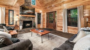 L’intérieur d’une cabane en rondins, avec une cheminée, des murs en bois, un ventilateur de plafond et une grande fenêtre.