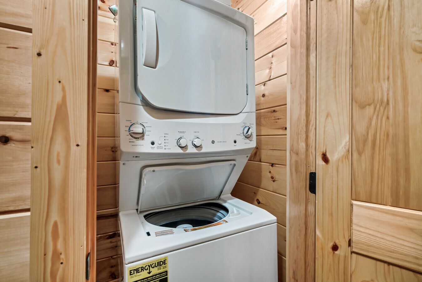 Un lavadero pequeño y funcional con dos puertas, paredes de madera y una lavadora blanca.