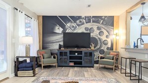 A living room with a large flat-screen TV, a wooden coffee table, two armchairs, a sofa, and a patterned rug.