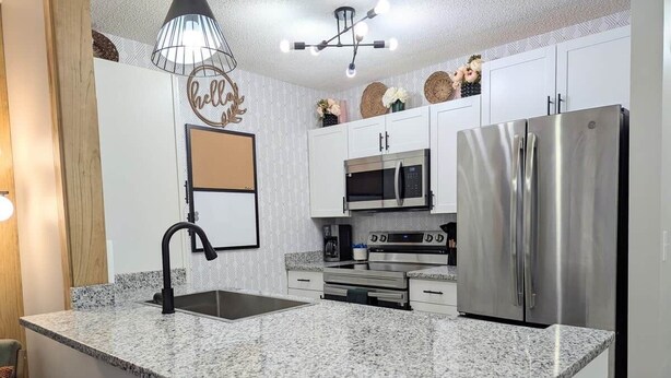 A kitchen with granite countertops, stainless steel appliances, and a pendant light.
