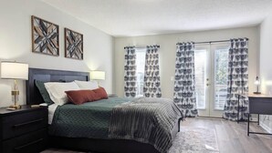 A bedroom with a bed, nightstands, a desk, and a window with curtains.