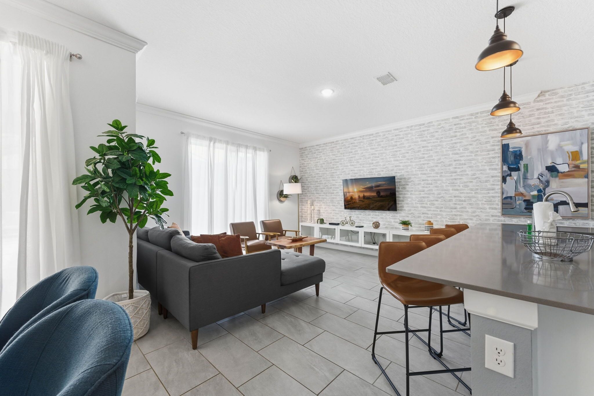 A modern living room with a grey sofa, blue chairs, a dining area with a bar, and a large plant.