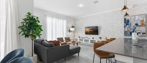 A modern living room with a grey sofa, blue chairs, a dining area with a bar, and a large plant.