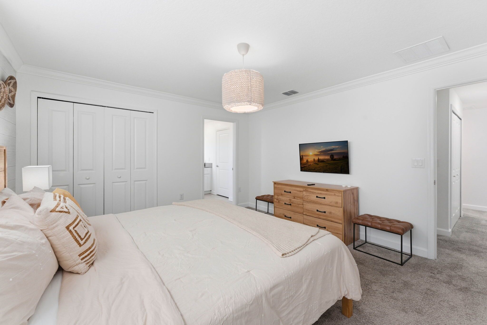 Un dormitorio con una cama grande, un aparador de madera, un banco, un televisor y una puerta que da a otra habitación.