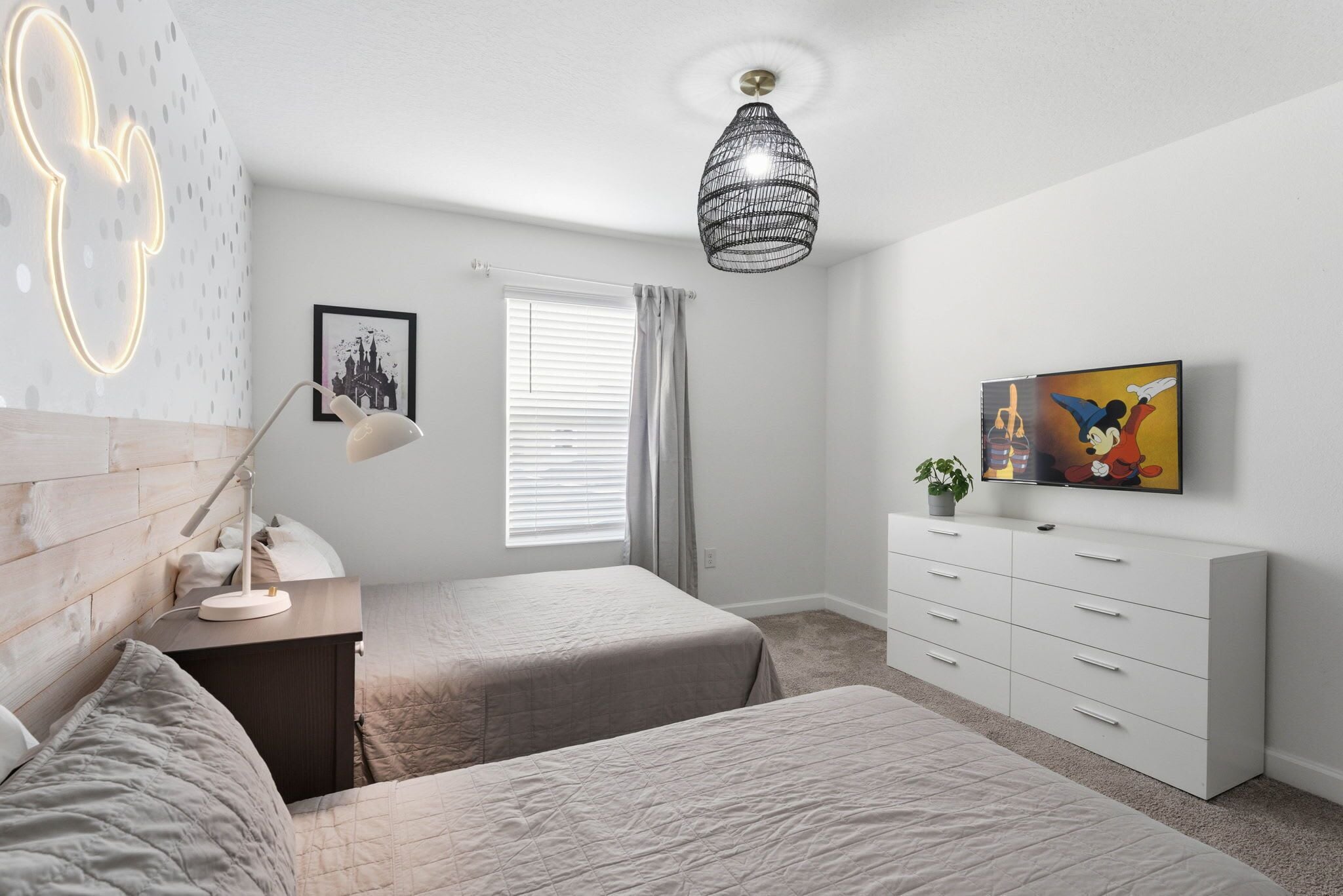 Une chambre avec deux lits, une table de chevet avec une lampe, une commode, un téléviseur fixé au mur et un luminaire au plafond.