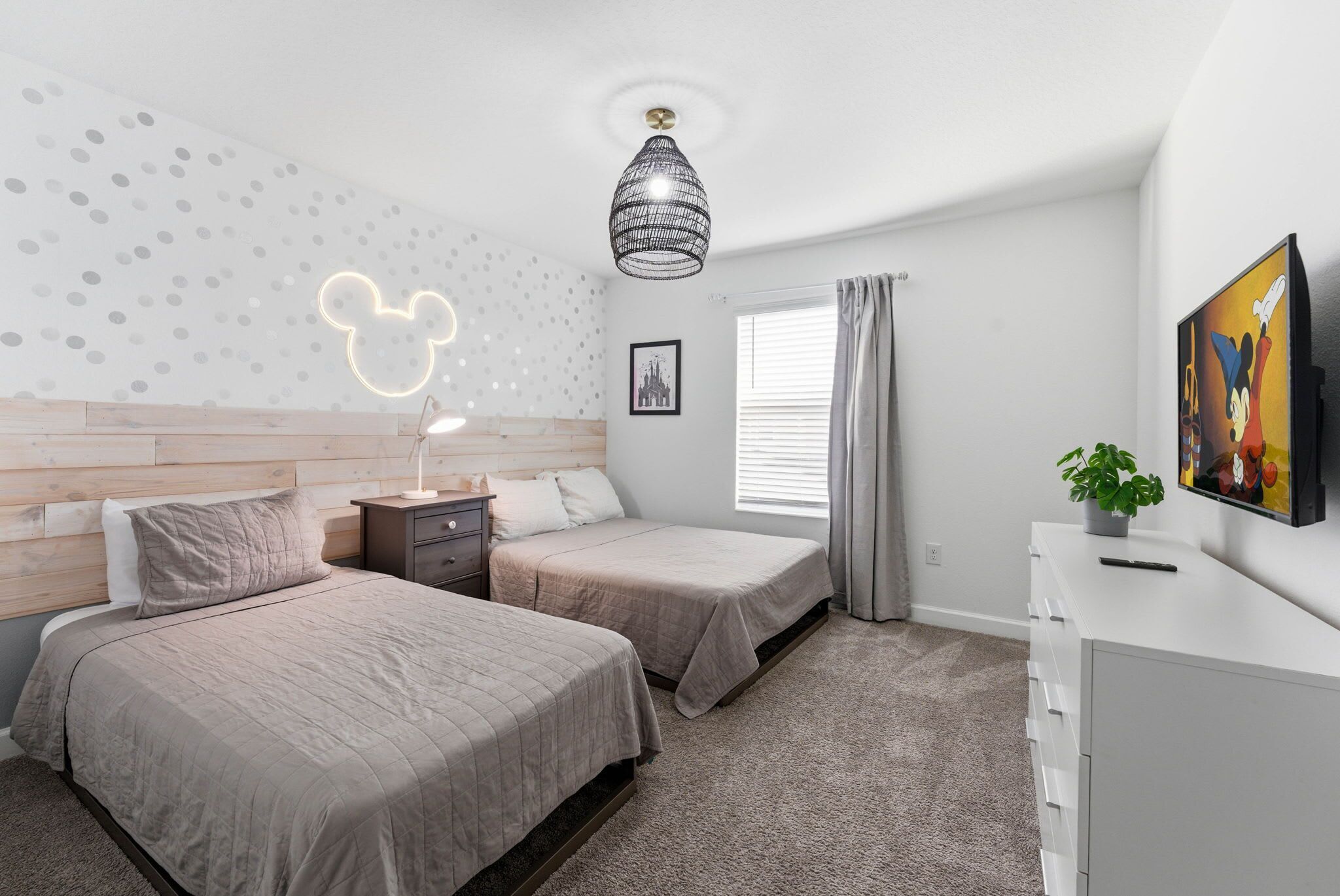 Ein Schlafzimmer mit zwei Betten, einem Nachttisch, einer Kommode, einer Mickey Mouse Lampe, einem Bilderrahmen und einem Fenster mit Vorhängen.