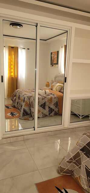 Un dormitorio con cama, mesita de noche, lámpara y ventana con cortinas.
