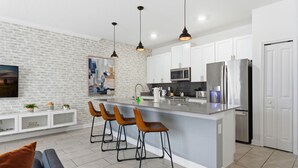 A modern kitchen with a central island, white cabinets, stainless steel appliances, and pendant lighting. - Chic 4BR Disney Retreat With Pool Mickey Rooms (Kissimmee)