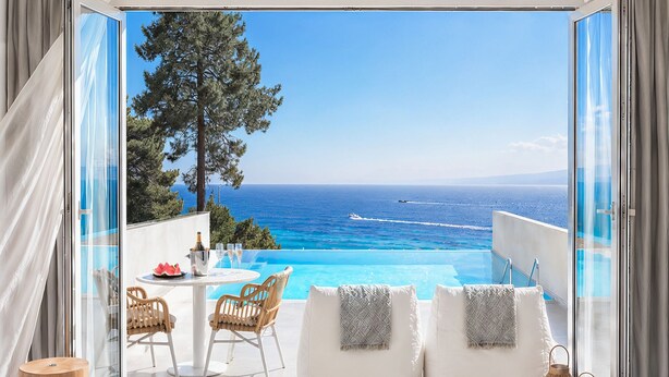 A bedroom with a large bed, a view of the sea, and a balcony with a table and chairs.