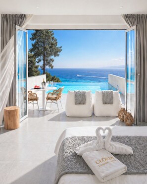A bedroom with a large bed, a view of the sea, and a balcony with a table and chairs. - Gloria Luxury Suites (Kassandra)