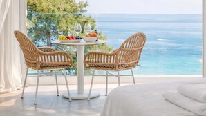 A balcony with wicker chairs, a round table with fruit and glasses, and a view of the ocean.