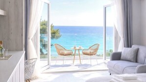 A bedroom with a large bed, a sofa, a dining table with chairs, and a view of the sea.