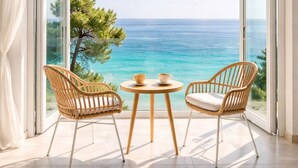A balcony with wicker chairs, a small round table, and a view of the sea.