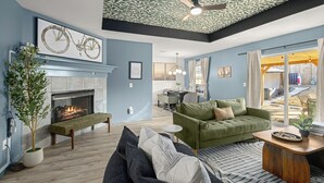 Un salon avec une cheminée, un canapé vert, un coin repas et une vue sur l’extérieur.