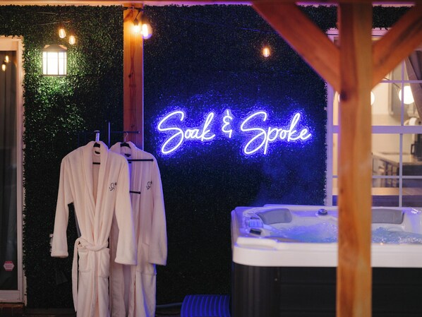 Kylpyläalue, jossa on pyyhetelineessä kaksi kylpytakia, neonvalomainos, jossa lukee ”Soak & Spoke”, ja taustalla poreallas.