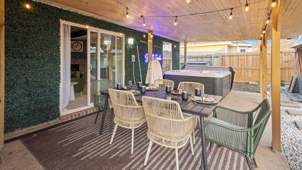 Une terrasse extérieure dotée d’un jacuzzi, de fauteuils en osier et de guirlandes lumineuses.
