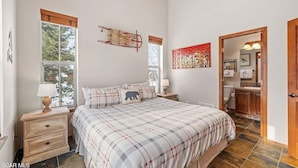 Quarto com cama grande, mesa de cabeceira, janela e porta para um banheiro.