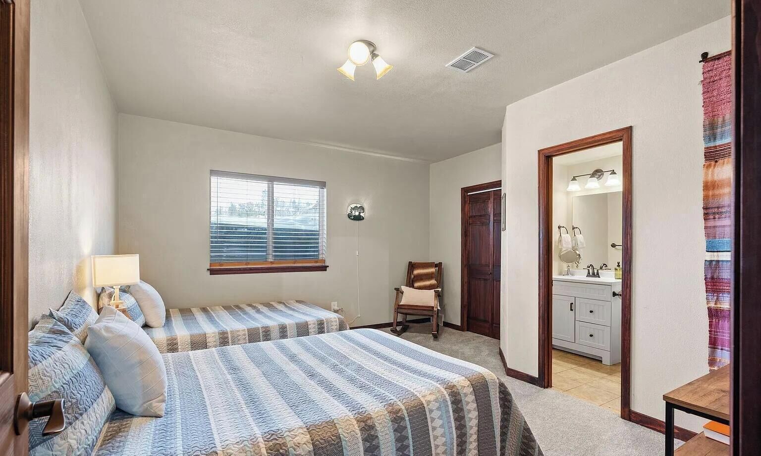 A bedroom with two beds, a window, a chair, a dresser, and a mirror.