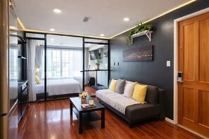 Una habitación de hotel moderna con sofá, una mesa de centro, un televisor y un cuadro de paisaje urbano.