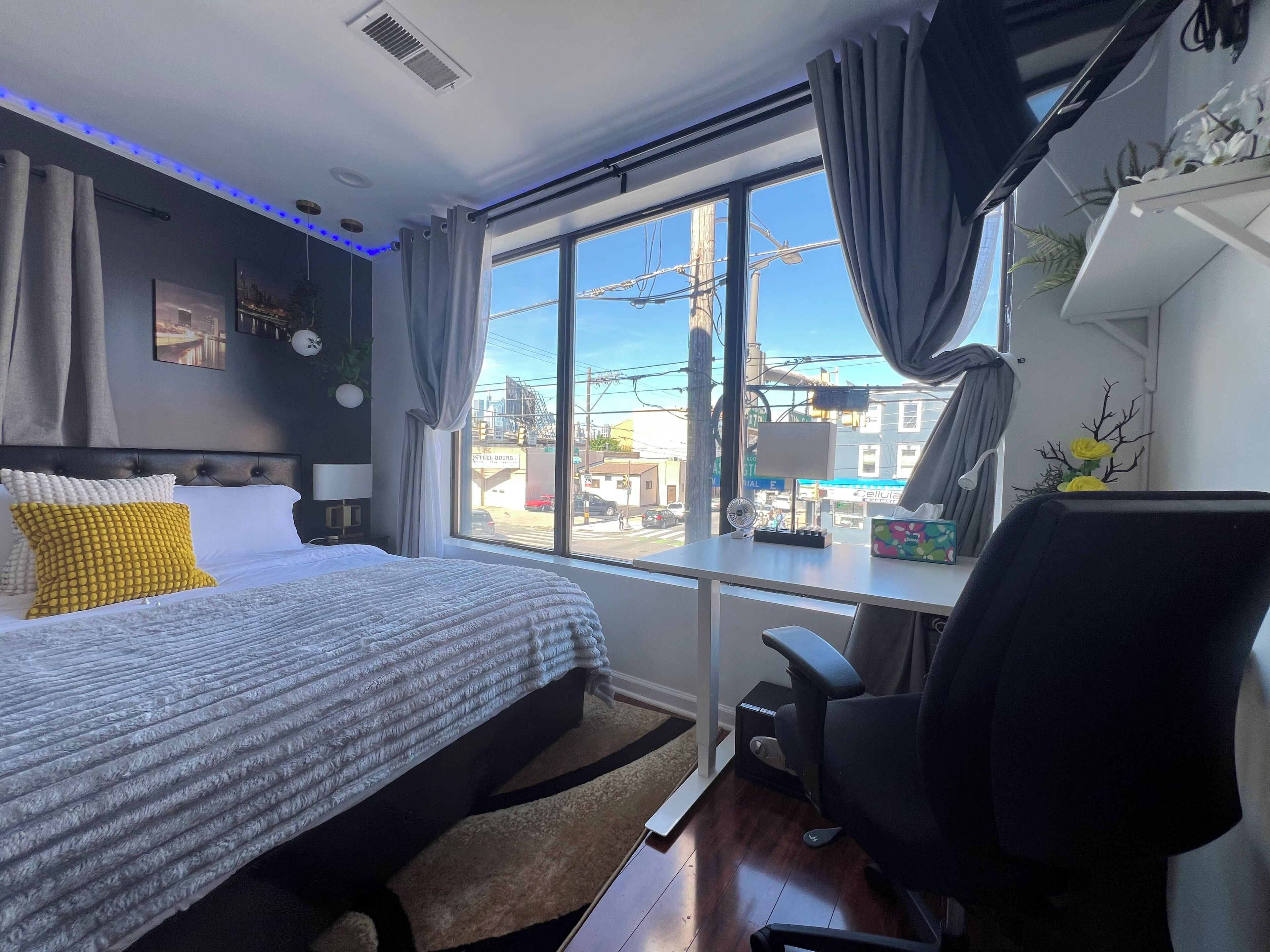 Une chambre d’hôtel moderne dotée d’un grand lit, d’un bureau avec une chaise, d’une vue sur la ville grâce à une grande fenêtre et d’un plafond orné de lumières LED bleues.