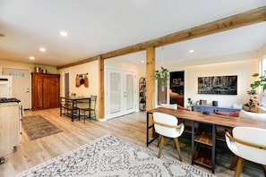 A spacious room with a wooden dining table, chairs, a kitchen area, and a large window.