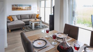 A modern living room with a sofa, dining table set for two, and a large window with a view of a field. - Lovely home in Butjadingen with sauna (Butjadingen)