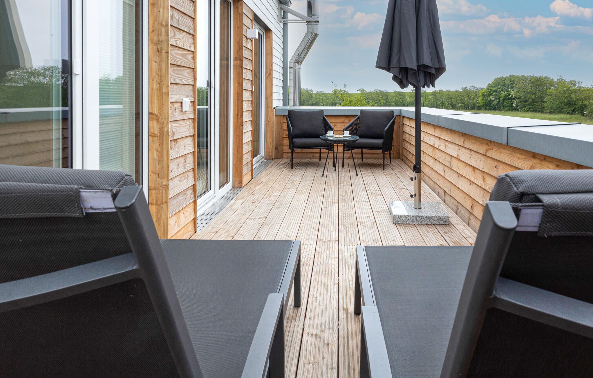 Una terraza de madera con dos sillones y una mesa, con vistas a un paisaje verde.