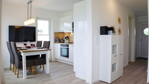 A modern kitchen with white cabinets, a built-in oven, and a dining area with a table and chairs. - Lovely home in Butjadingen with sauna (Butjadingen)