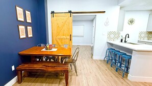 Un comedor con mesa y sillas de madera, una cocina con taburetes de bar azules y una puerta corredera estilo granero.