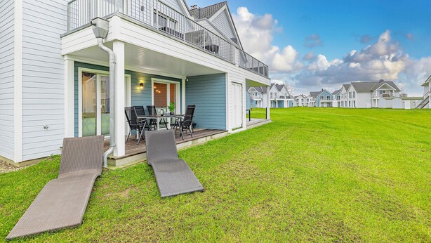 Een modern huis met een overdekte veranda, een eethoek en een verzorgd gazon.
