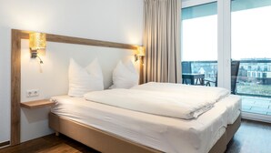 Camera d'albergo moderna con un letto grande, una testiera in legno, lampade sui comodini e vista sulla città attraverso ampie finestre.