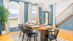 Uma sala de jantar com uma mesa de madeira posta para seis pessoas, rodeada por cadeiras pretas, um candelabro e um vaso de planta.