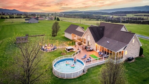 Uma casa grande com piscina, área de estar externa e vista para o campo.