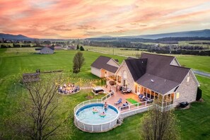 A large house with a swimming pool, outdoor seating, and a view of the countryside. - Pet-Friendly · Heated Pool · Hot Tub · Arcade · Movie Room · Epic Views & more! (Luray)