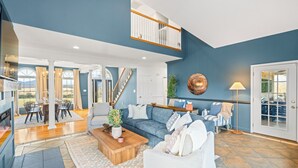 Uma sala de estar ampla com parede azul, mesa de centro de madeira, sofá branco e um espaço de jantar com mesa e cadeiras.