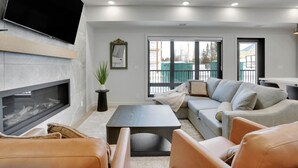 A modern living room with a fireplace, a sofa set, a coffee table, and a flat-screen TV mounted on the wall. - 3 Bedroom with Outdoor Heated Pool and Hottub! (Canmore)