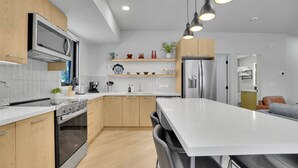 A modern kitchen with wooden cabinets, stainless steel appliances, a central island, and pendant lighting. - 3 Bedroom with Outdoor Heated Pool and Hottub! (Canmore)